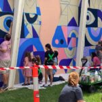 Children and adults painting a large colorful mural together during a community art event.